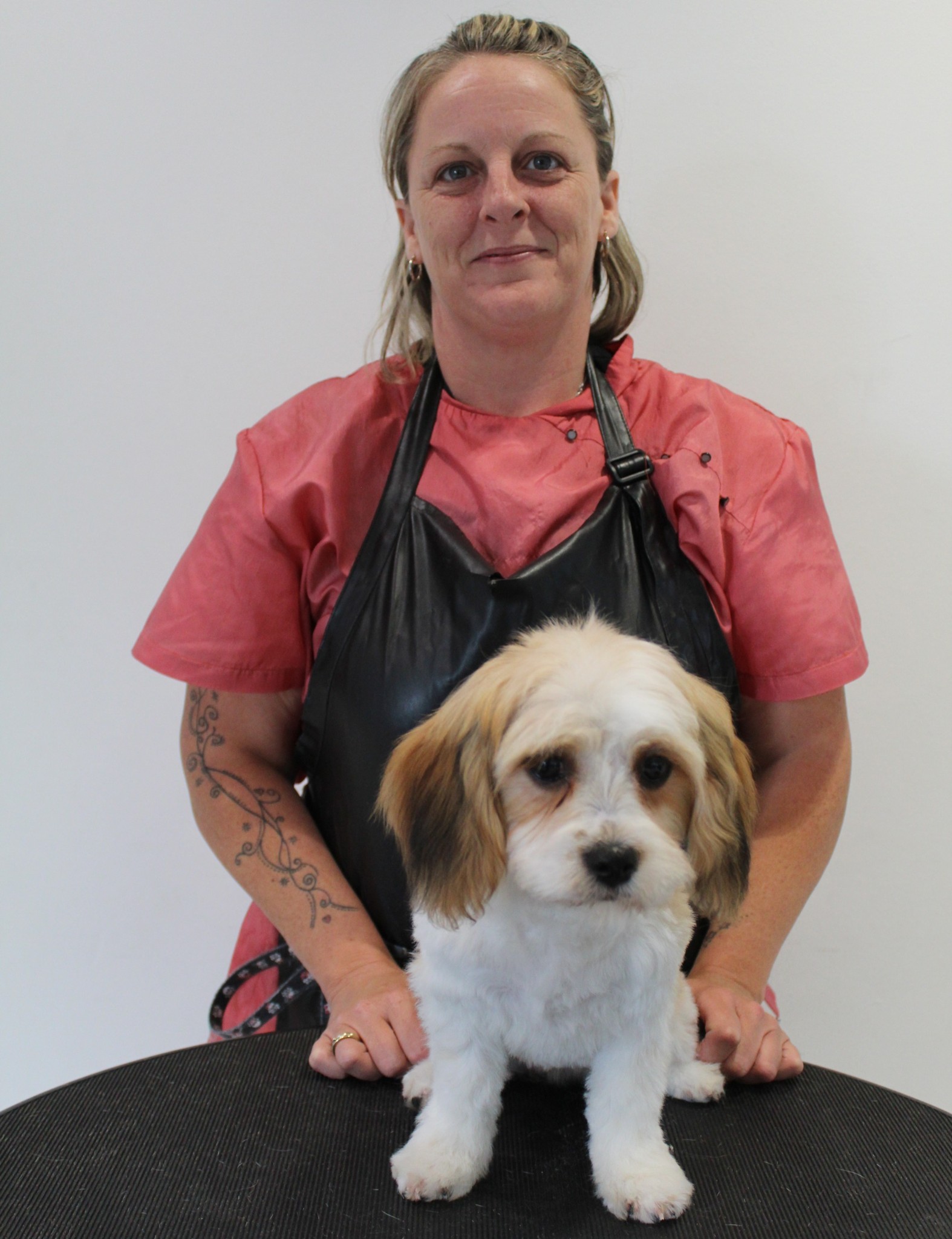 Sonia holding a small cream and white puppy on the grooming table